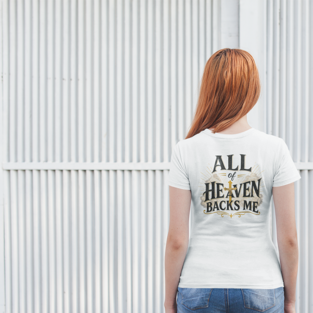Person wearing a white t-shirt with 'All of Heaven Backs Me' text, standing against a corrugated metal wall.