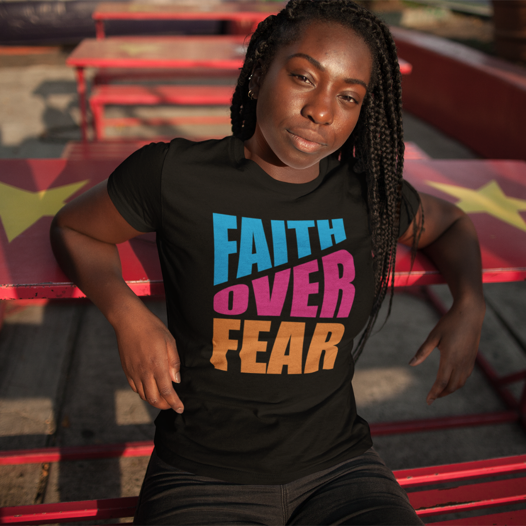Person wearing a black t-shirt with 'Faith Over Fear' text in colorful letters, sitting on a red bench.