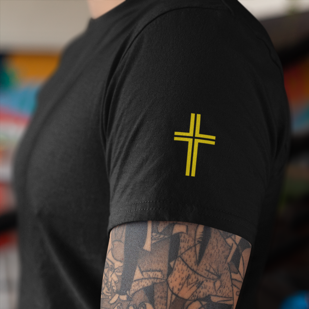Person wearing a black t-shirt with a yellow cross design on the sleeve.