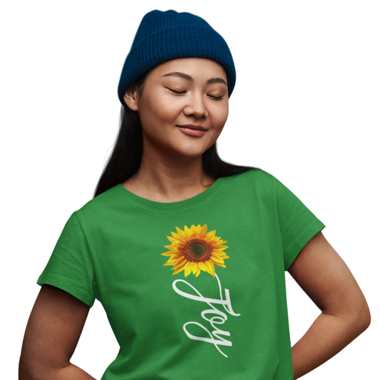Person wearing a green t-shirt with a sunflower and 'Joy' text, blue beanie on white background