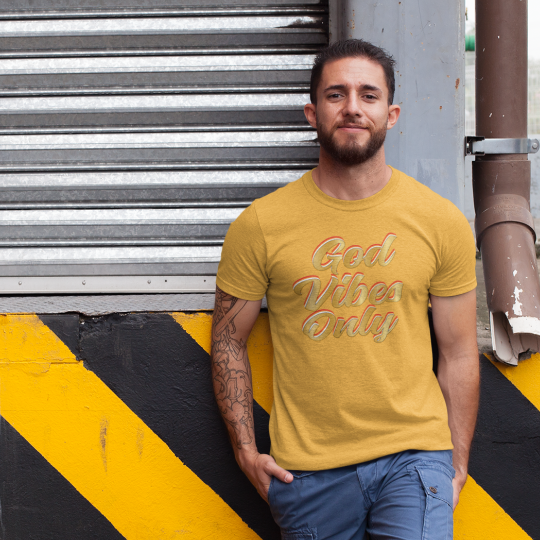 Man wearing a yellow t-shirt with 'God Vibes Only' text standing against a metal shutter.