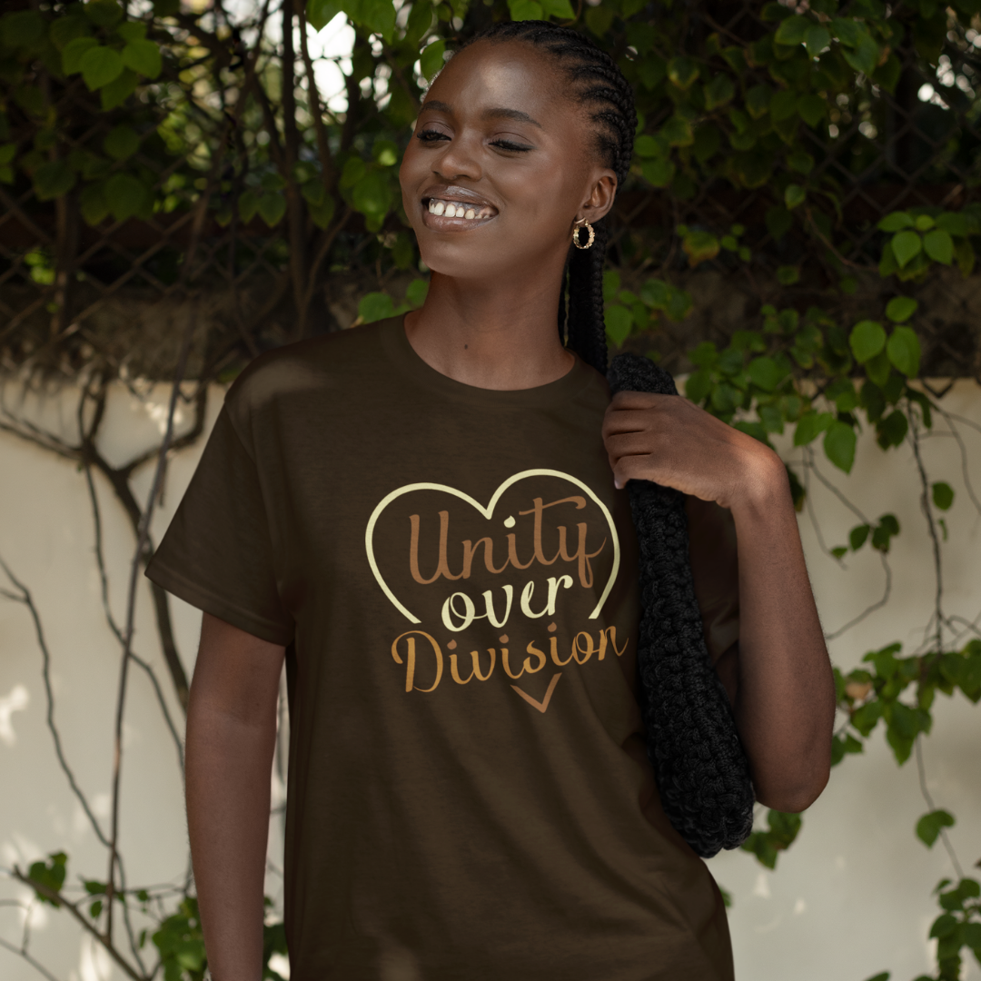 Woman wearing a brown t-shirt with 'Unity over Division' text, standing outdoors with greenery.