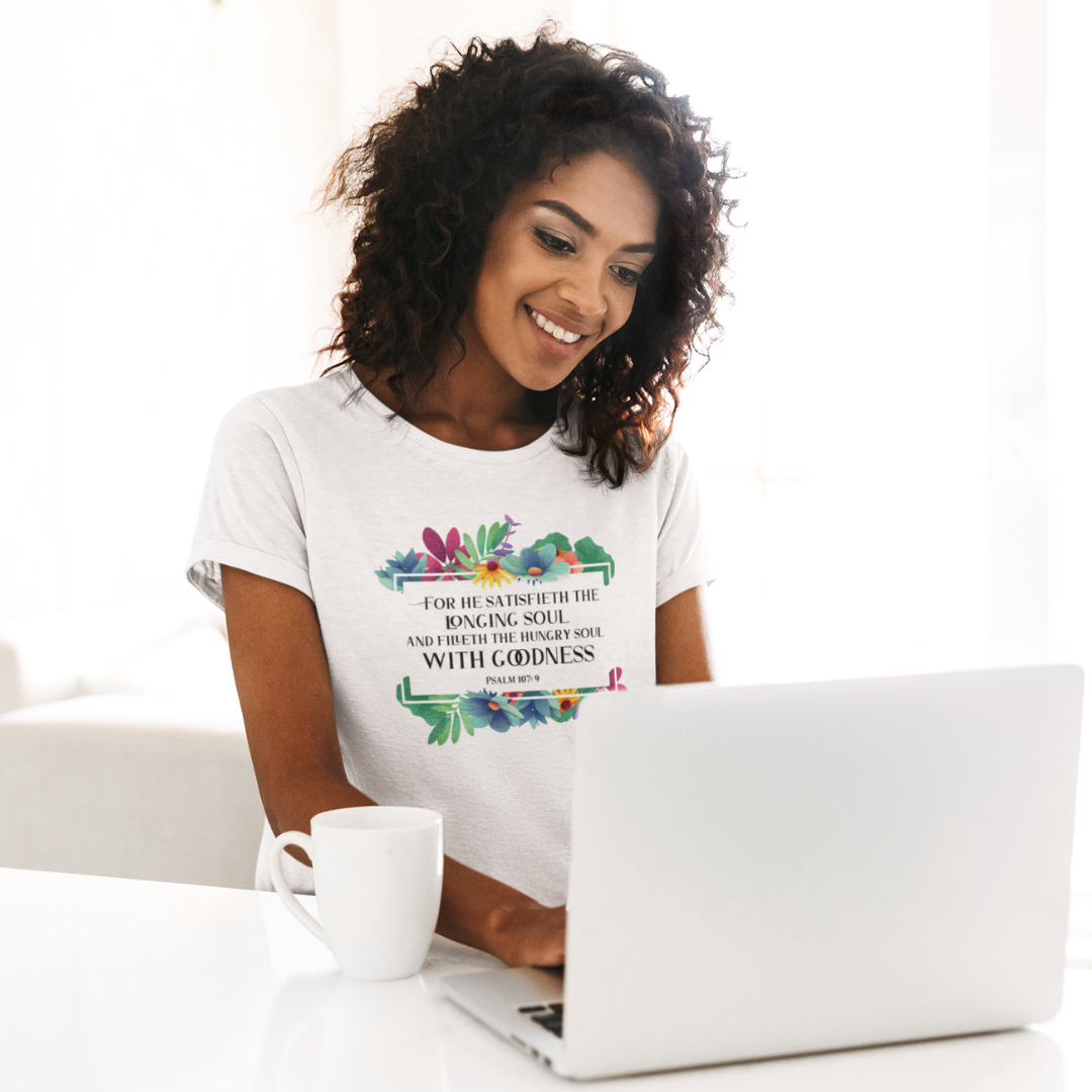 Woman wearing a white t-shirt with colorful text and design, sitting at a table with a laptop and mug.
