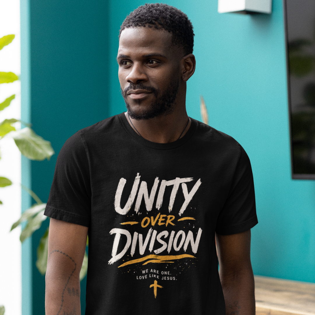 Man wearing a black t-shirt with 'Unity Over Division' text, standing against a teal wall.